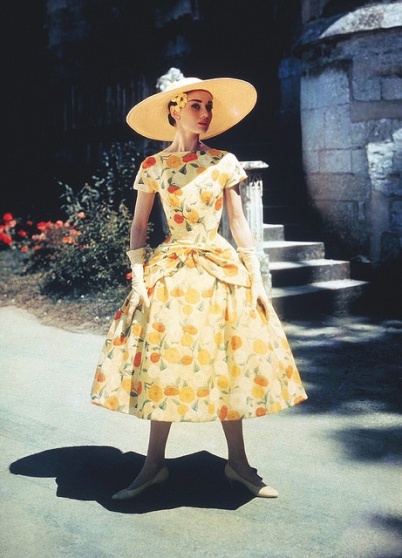 segue un abito dal taglio molto simile al primo, ma con maniche corte e fantasia a fiori sul bianco e giallo, portato con un cappello di paglia a tesa larga. In questo scatto, Audrey è ritratta con un enorme mazzo di fiori in una fioreria.